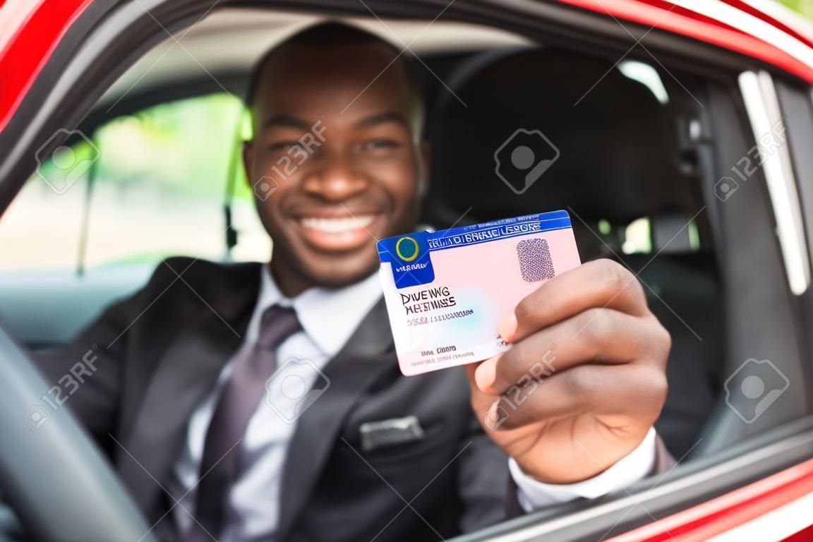 Feliz hombre de negocios africano joven que muestra su licencia de conducción De Abrir la ventana de coche