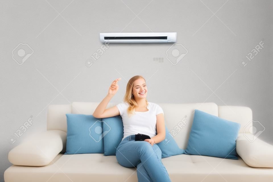 年轻快乐的女人坐在沙发上用遥控器在家里操作空调
