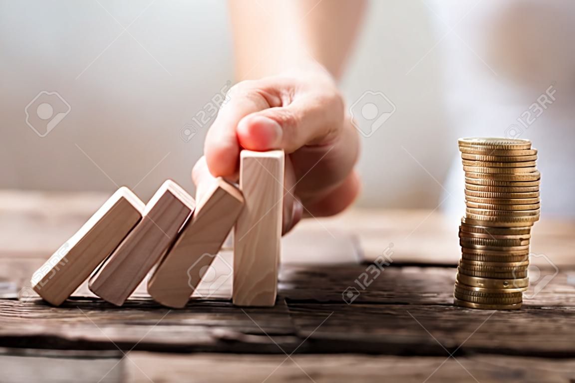 Close-up van de hand van een zakenvrouw het stoppen van de houten blokken van vallen op gestapelde munten