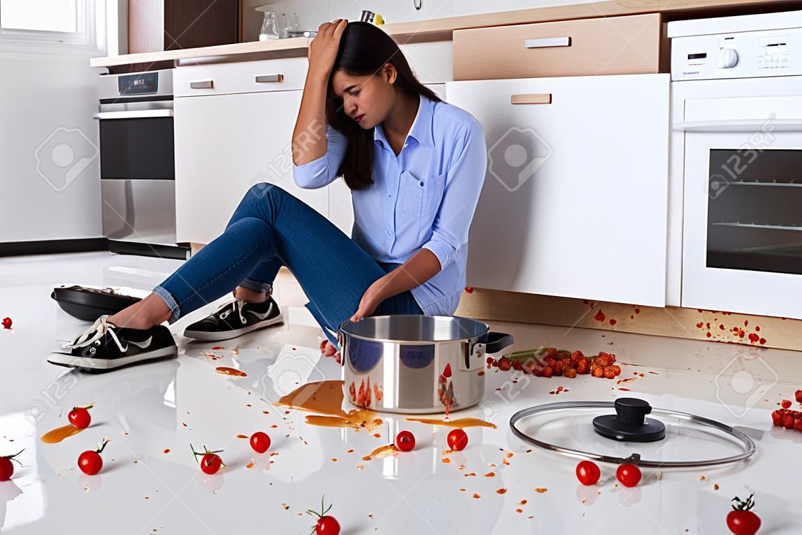 Unhappy Woman Sitting On Kitchen Floor With Spilled Food In Kitchen