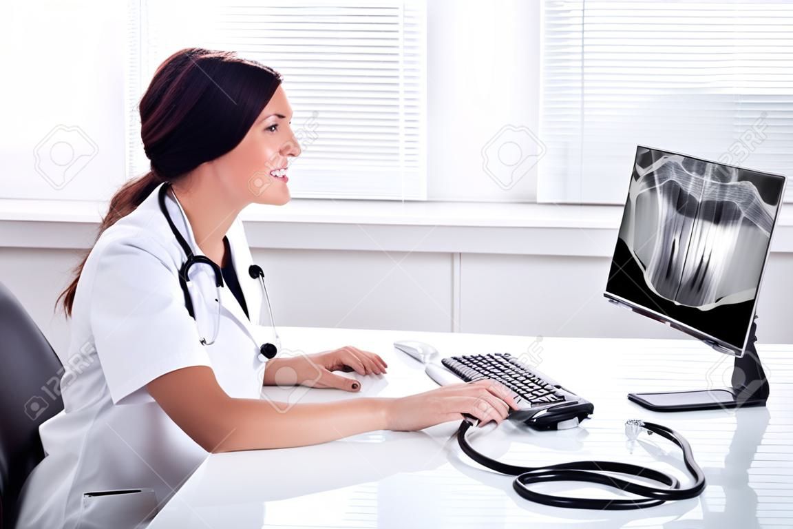 Female Doctor Looking At Teeth X-ray On Computer Over Desk In Clinic
