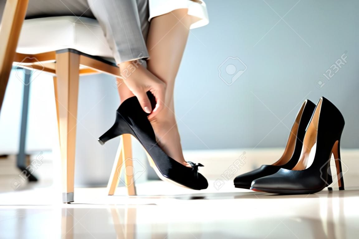 Seção baixa da mulher de negócios que muda o calçado do salto alto aos sapatos confortáveis no escritório