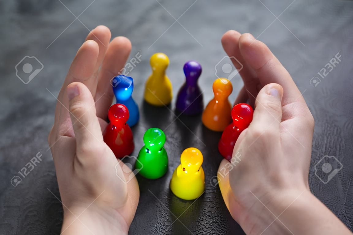 Close-up Of A Person's Hand Protecting Multicolored Pawns Forming Circle Over White Desk
