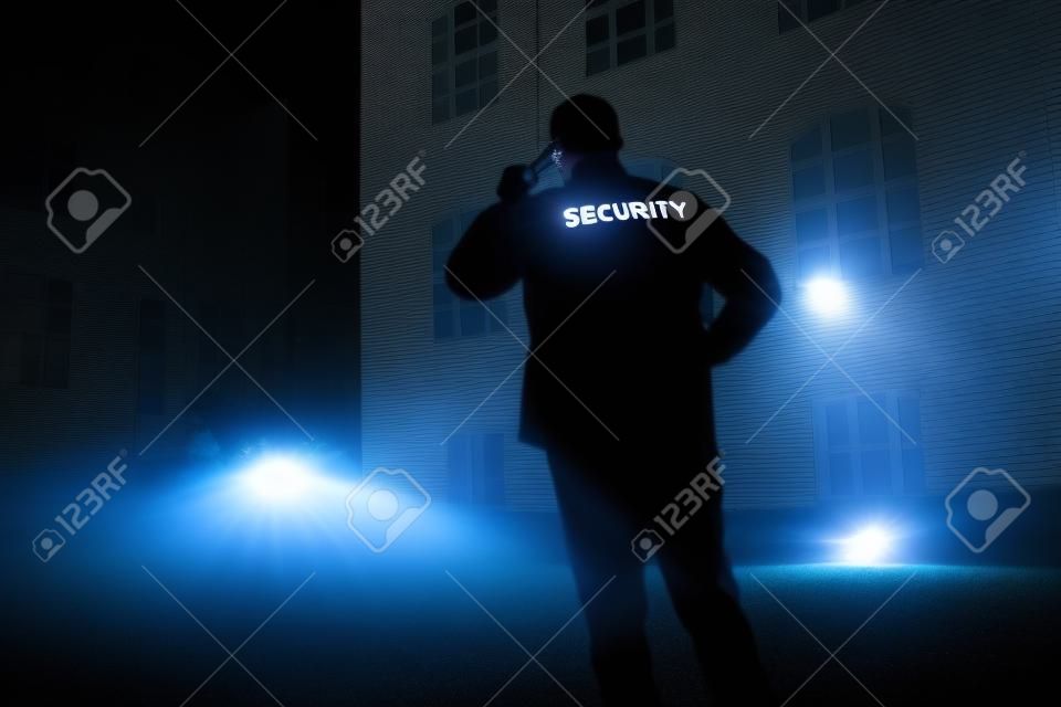 Strażnik spacerujący po obwodzie budynku z latarką w nocy