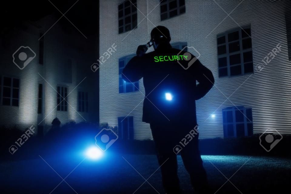 Strażnik spacerujący po obwodzie budynku z latarką w nocy