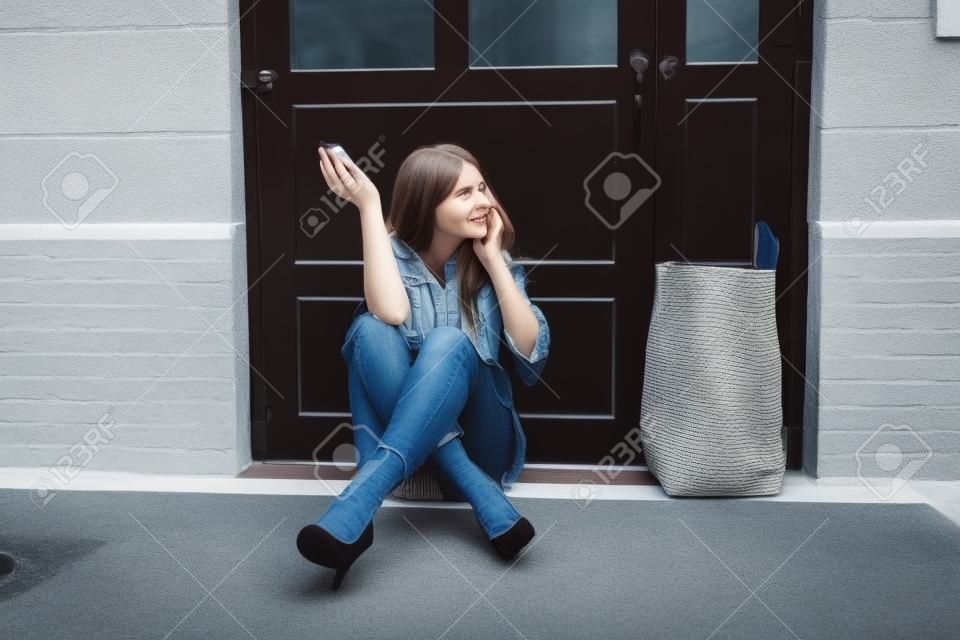 Een bange jonge vrouw die buiten de deur zit te praten op de mobiele telefoon