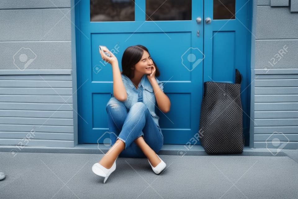 Una mujer joven asustada sentada afuera de la puerta hablando por teléfono móvil