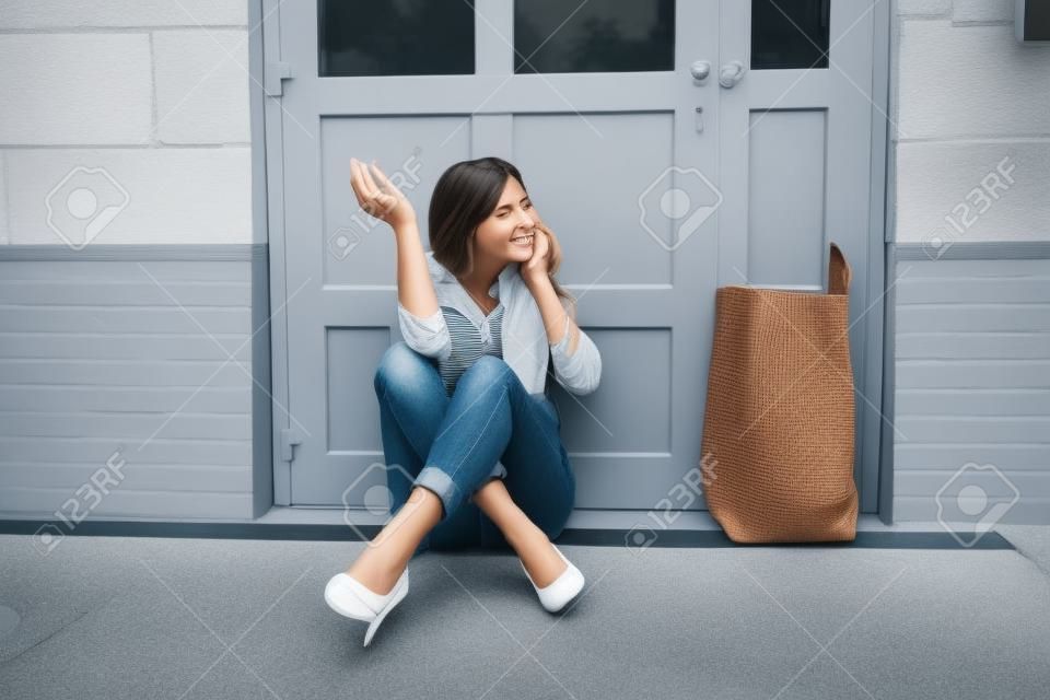 Une jeune femme effrayée s'asseyant en dehors de la porte parlant sur le téléphone portable