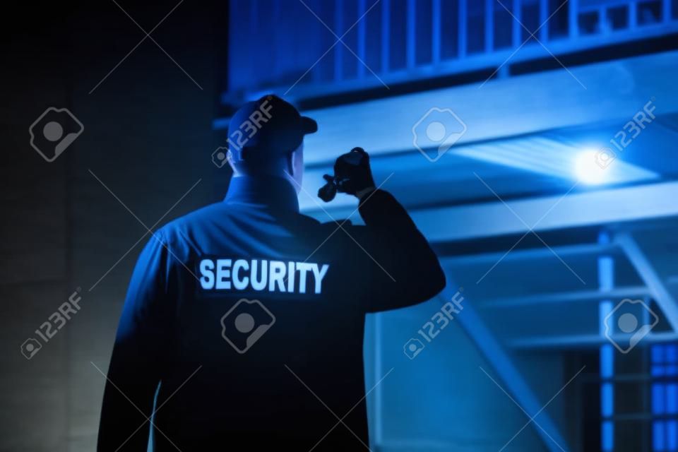 Security Guard Walking Building Perimeter With Flashlight At Night