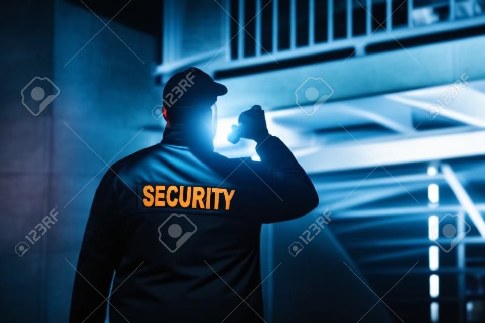 Guardia de seguridad caminando por el perímetro del edificio con linterna por la noche