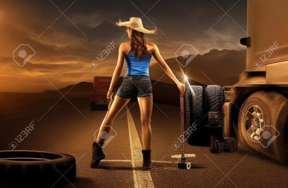아름다운 여성 트럭 운전사는 도로의 바퀴에 타이어를 교체합니다.