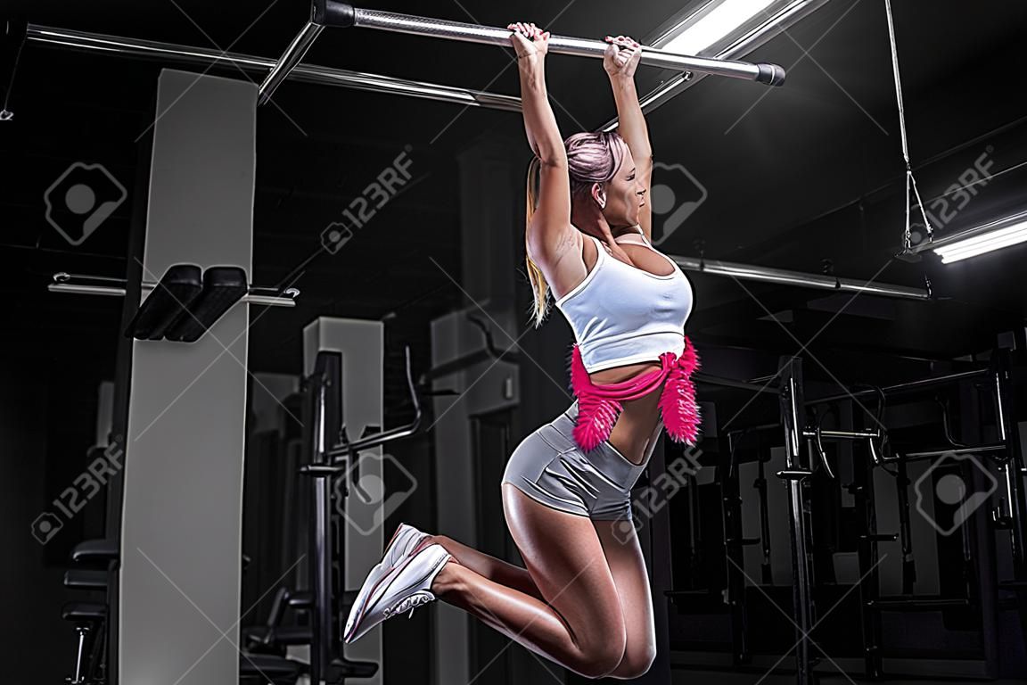 Attraktives vollbusiges Girl zieht sich an der Stange hoch. Fitness- und Bodybuilding-Konzept. Gemischte Medien