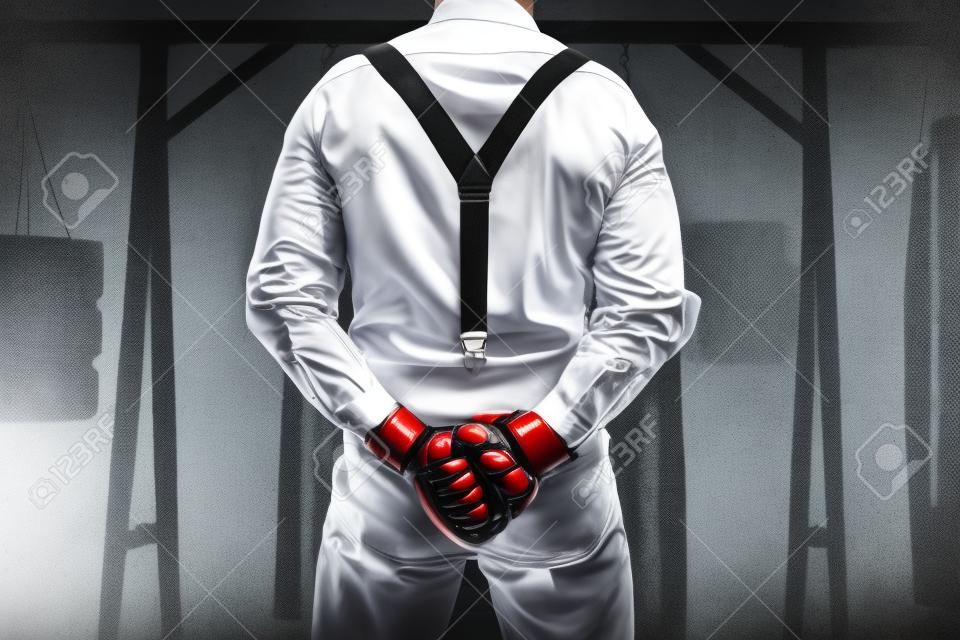 Image of a brutal man in a white shirt and suspenders standing in the gym with his back to the camera. Mixed martial arts. The concept of fist fights. Mixed media