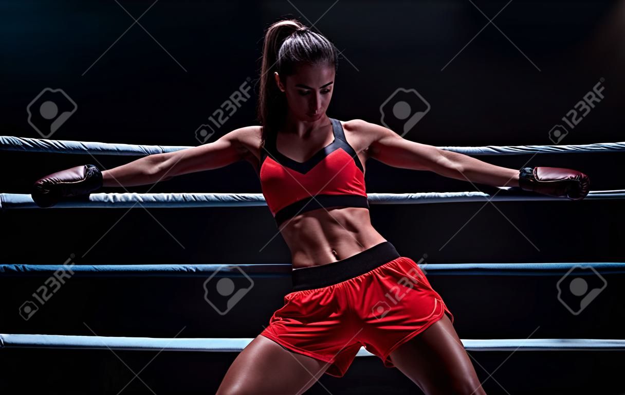 Atletische vrouw in rode shorts en top poseren in de ring. Boksen en gemengde vechtsport concept. gemengde media