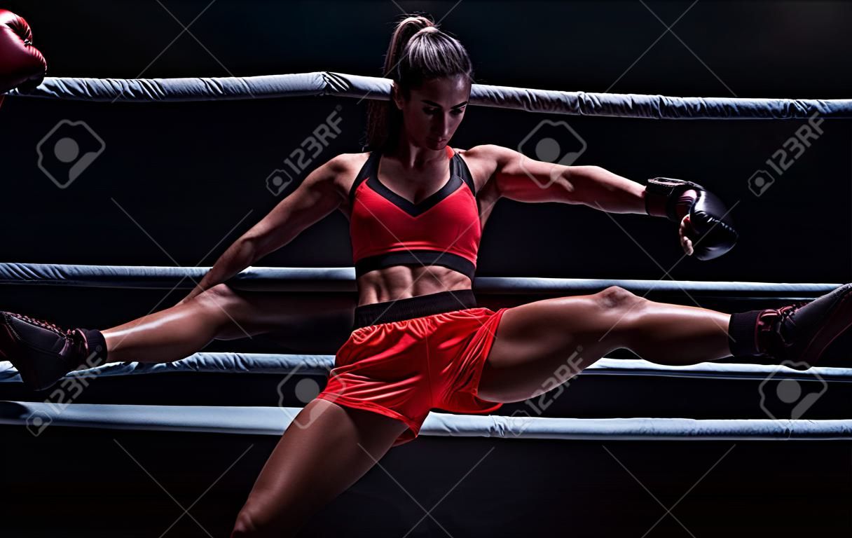 Atletische vrouw in rode shorts en top poseren in de ring. Boksen en gemengde vechtsport concept. gemengde media