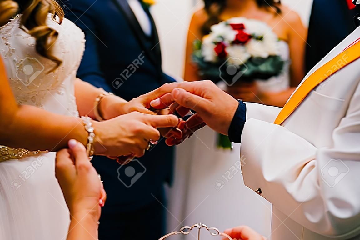 Priest putting golden ring on a bridegroom hand at wedding ceremony in church.