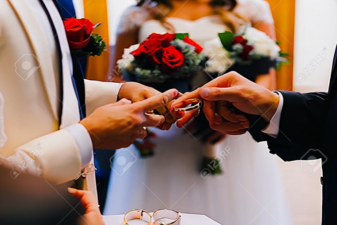 Priest putting golden ring on a bridegroom hand at wedding ceremony in church.