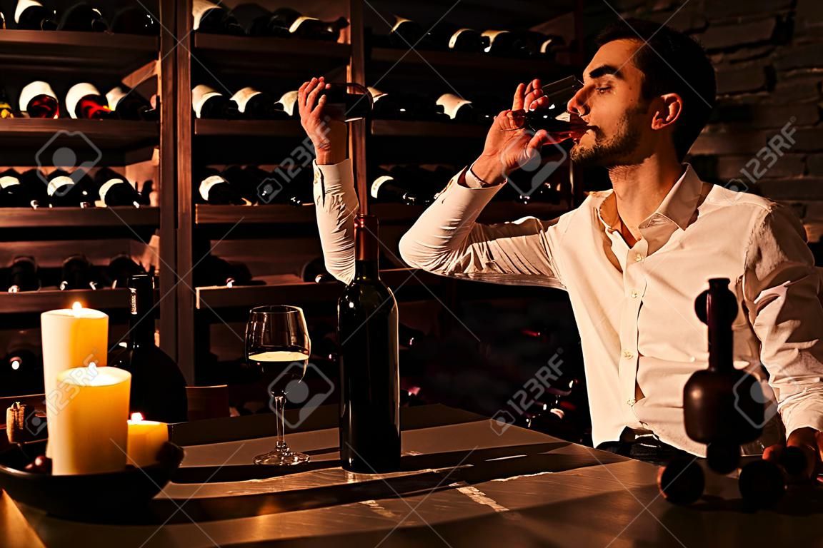 O homem está a provar vinho de um copo de vinho. Homem sentado à mesa num cofre de vinho.