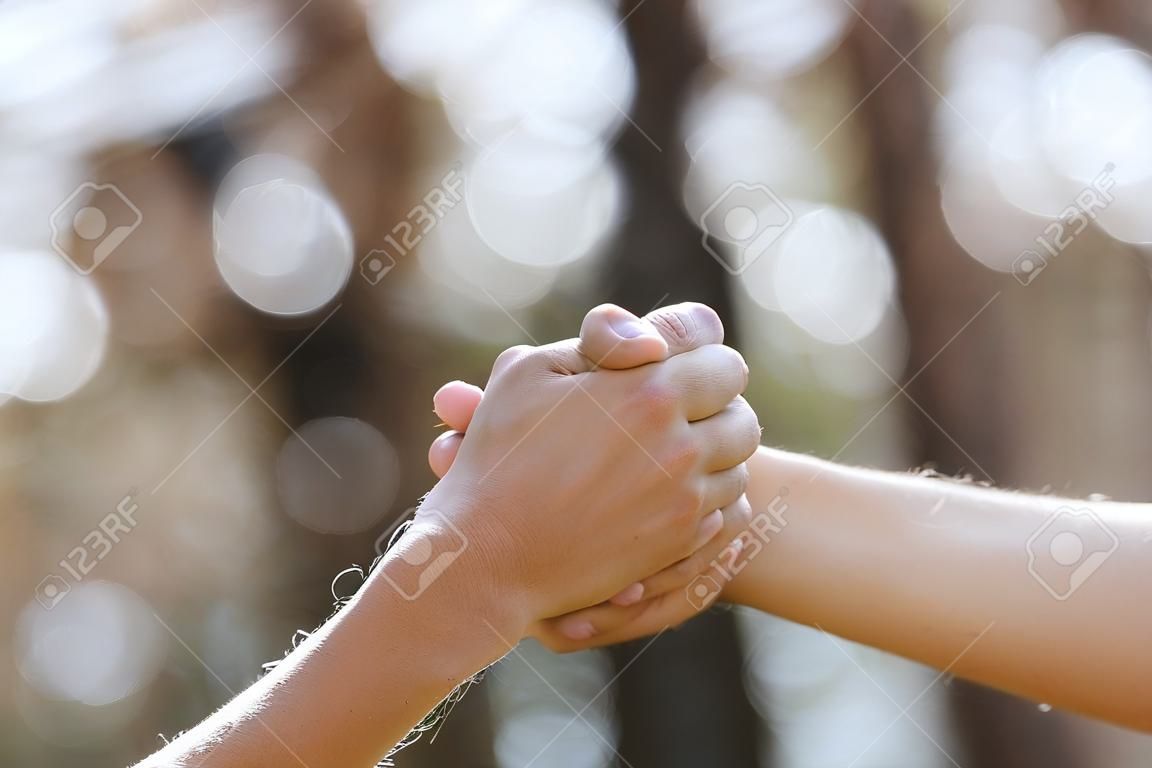 公園の自然な背景に孤立した握手をする2人。コラボレーションのシグナルを持つ2つの手を分離します。コピースペース。選択的フォーカス。