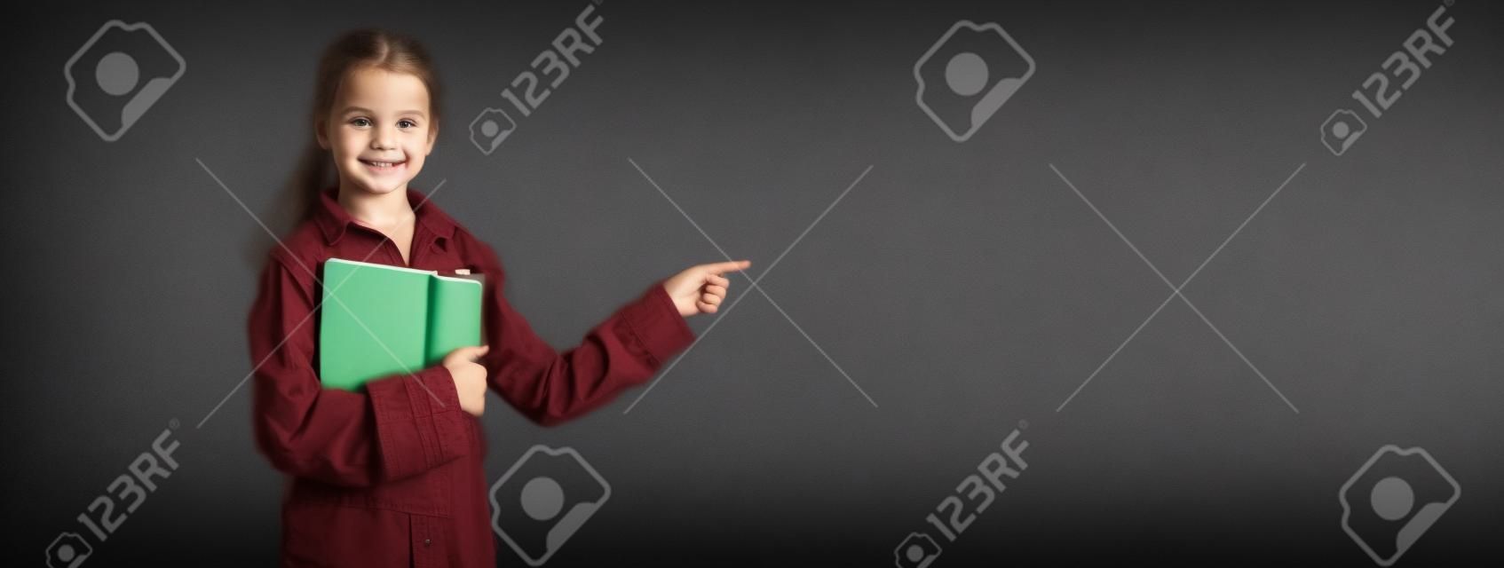caucasian girl student in the classroom near the chalk board. Holds a notebook smiling indicates an empty space for the text. Online education and e-learning concept. Back to school. banner.