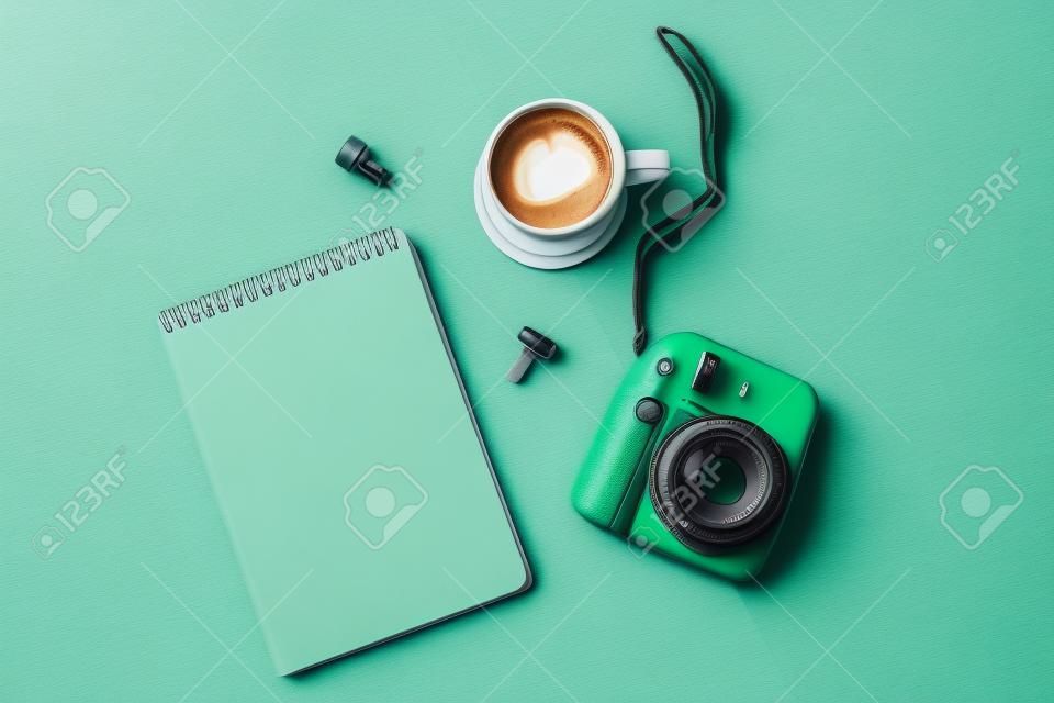 Flat lay with modern mini camera, empty notebook and cup of coffee on double grey green background. Top view, flat lay style composition. Fashion blogger, minimal concept
