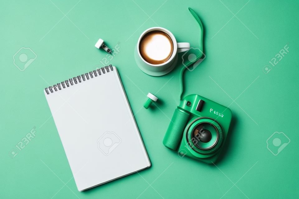 Flat lay with modern mini camera, empty notebook and cup of coffee on double grey green background. Top view, flat lay style composition. Fashion blogger, minimal concept