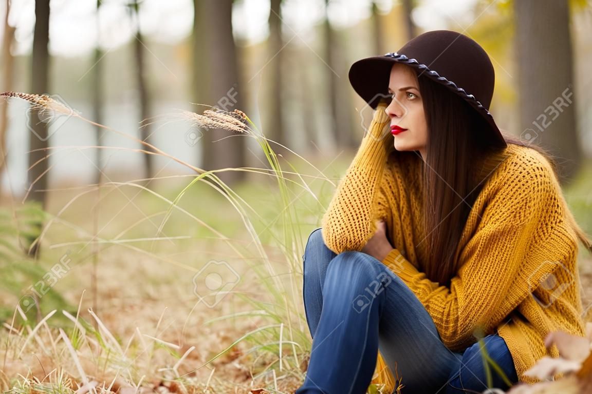 Samotna dziewczyna siedzi w lesie jesienią