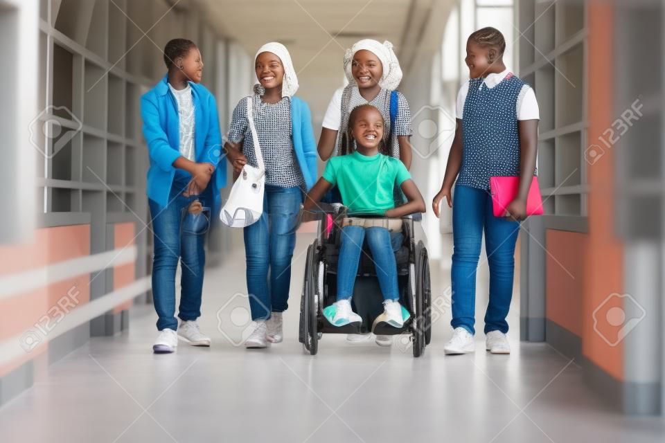 African girl in wheelchair chatting with her friends while they walking along the school corridor