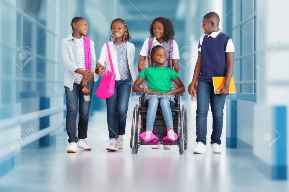Niña africana en silla de ruedas charlando con sus amigos mientras caminan por el pasillo de la escuela
