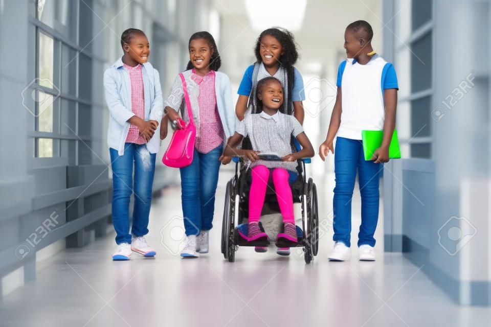 Afrikaanse meisje in rolstoel kletsen met haar vrienden terwijl ze lopen langs de school gang