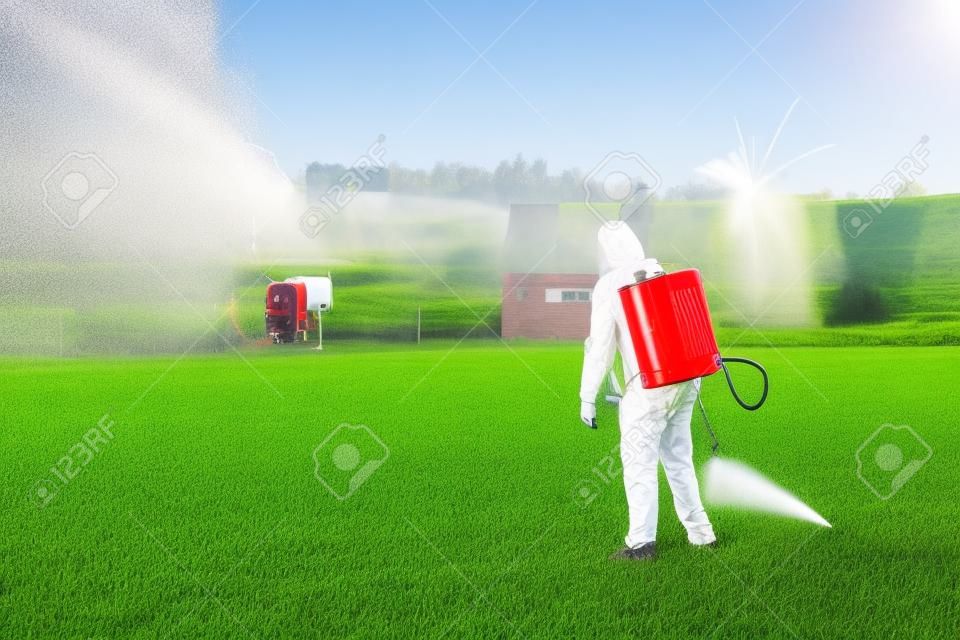 Farmers spraying pesticide on lawn field wearing protective clothing. Insecticide sprayer with a proper protection. Treatment of grass from weeds and dandelion. Copy space. Gardening care season. Man.