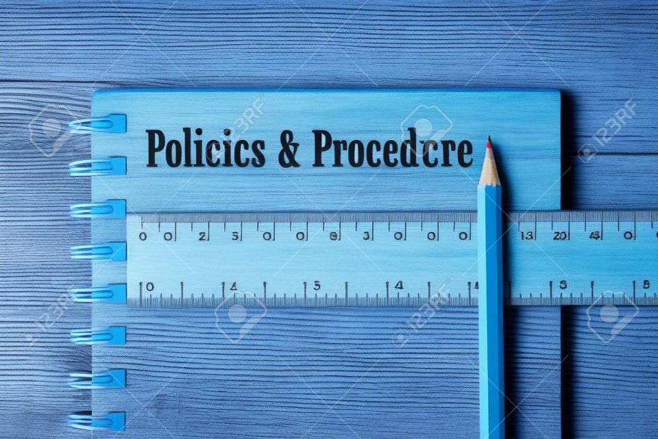 Policies & Procedure word on notebook, wooden ruler and pencil on blue wooden background. Top view.