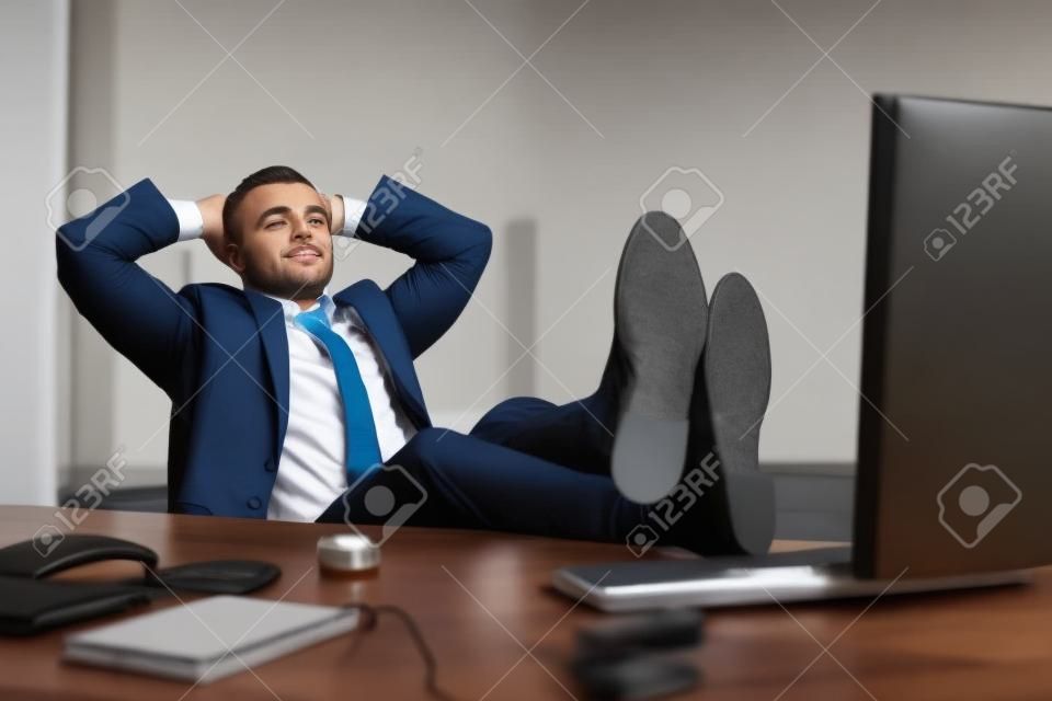 Hombre guapo empresa joven con los pies descansando sobre el escritorio