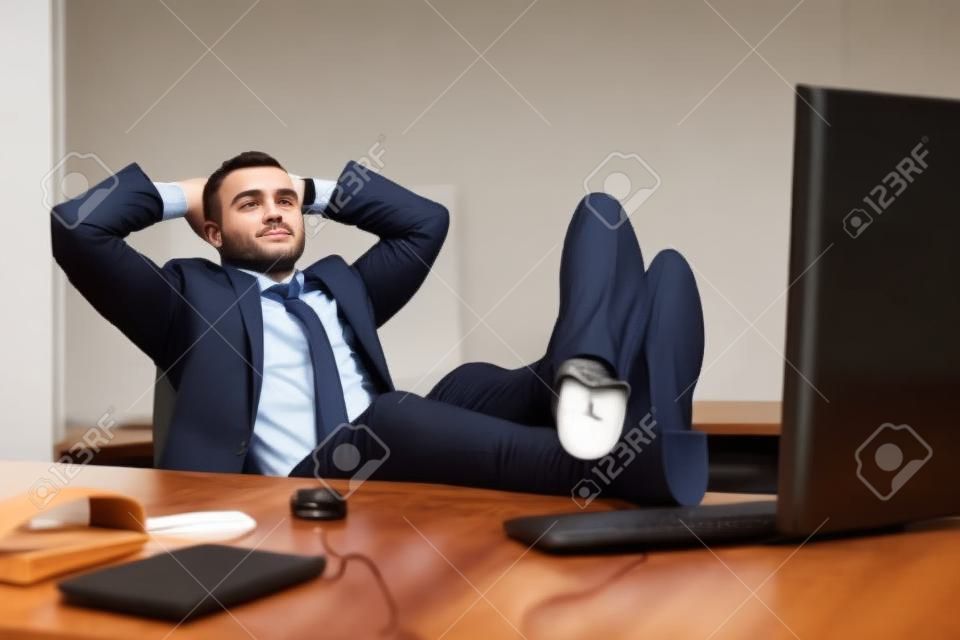 Hombre guapo empresa joven con los pies descansando sobre el escritorio