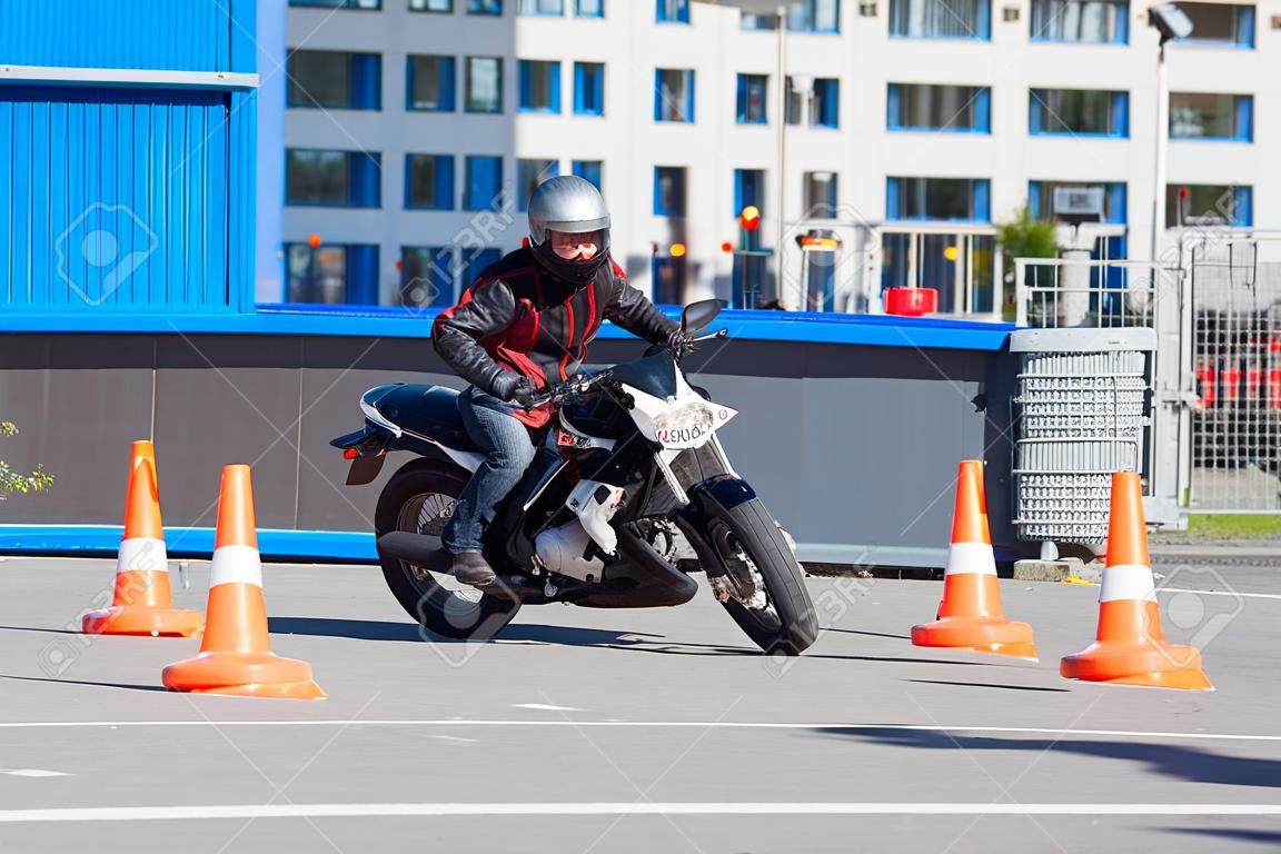 L-driver person drives slalom through the orange cones on motordrome on motorcycle