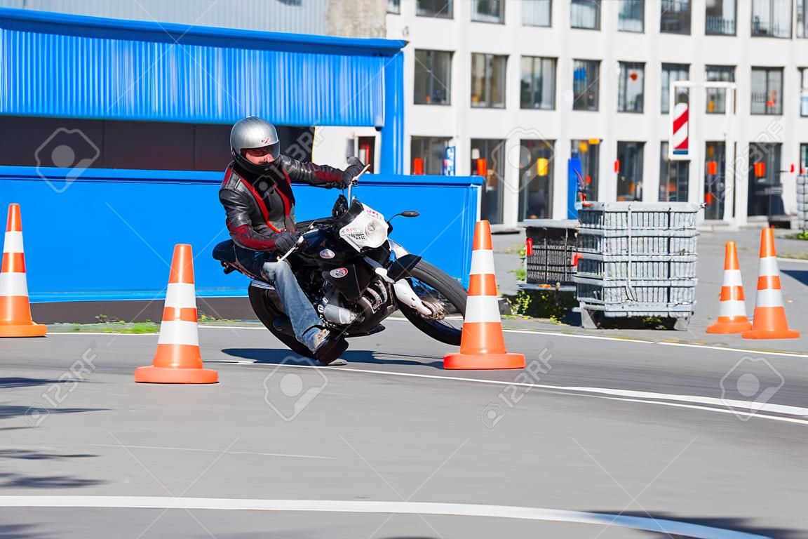 L-driver person drives slalom through the orange cones on motordrome on motorcycle