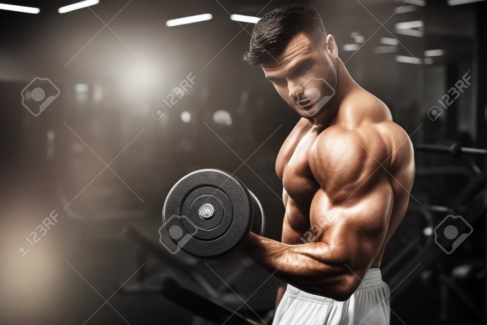 Beau jeune homme caucasien musclé en forme d'apparence de modèle entraînement d'entraînement dans la salle de gym prendre du poids en pompant des muscles, pose, boit de l'eau fitness et concept de nutrition sportive de musculation