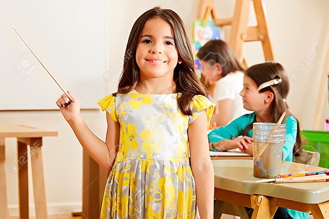Cute Hispanic little girl smiling in front of her classroom during art class