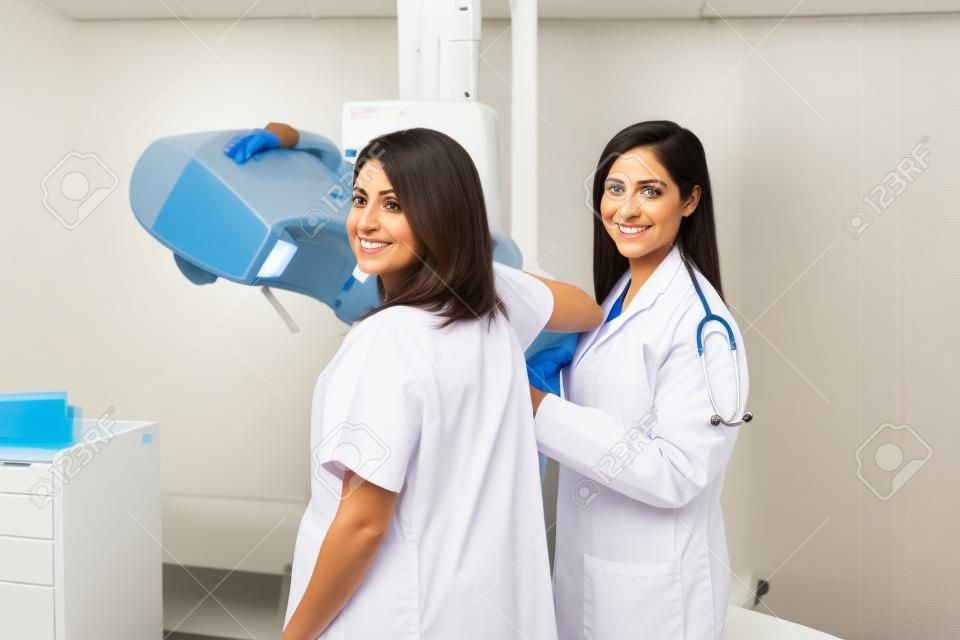 Porträt eines schönen hispanischen Patienten und ihres Doktors mitten in einer Mammographie in einem Krankenhaus