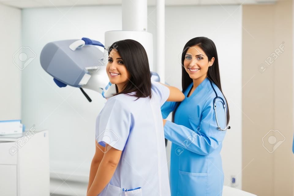 Porträt eines schönen hispanischen Patienten und ihres Doktors mitten in einer Mammographie in einem Krankenhaus