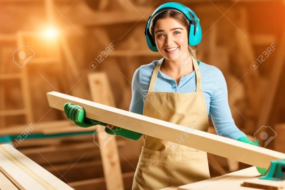 Schattig jonge vrouwelijke timmerman snijden wat hout in een tafelzaag en genieten van haar werk