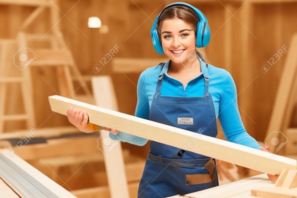 Jolie jeune femme charpentière coupant du bois dans une table vu et appréciant son travail
