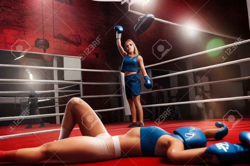 Good looking young woman looking at her defeated opponent after knocking her out on a box fight in a boxing gym