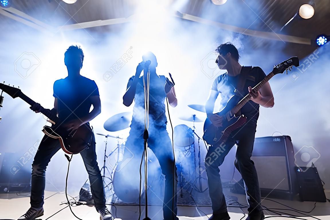 Rock and roll band members performing live on stage with lights and smoke