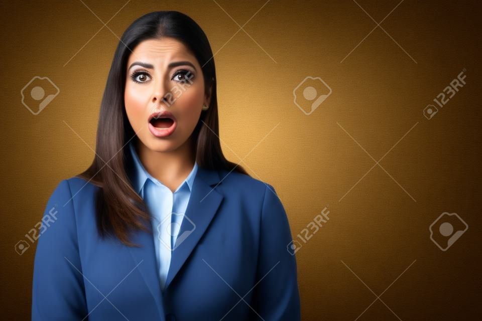 Beautiful Hispanic businesswoman standing with mouth open in shock at studio