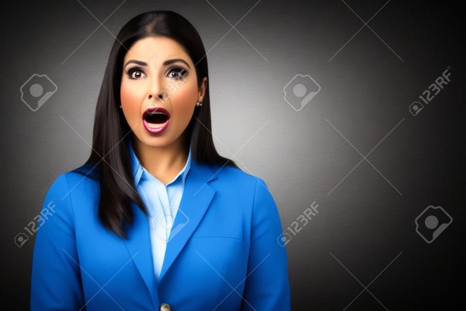 Beautiful Hispanic businesswoman standing with mouth open in shock at studio