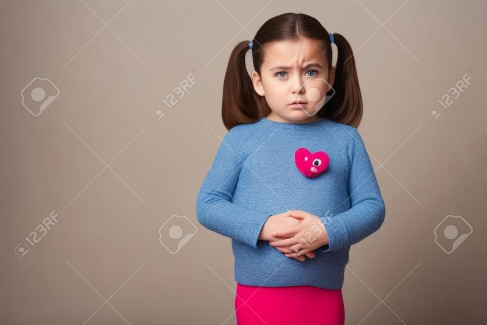 Serious looking little girl touching her belly and feeling sick with a stomachache in a studio