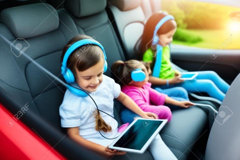 Hermosos niños viendo una película en una tableta con auriculares mientras están sentados en el auto. Hermanitos disfrutando de ir de viaje con sus padres