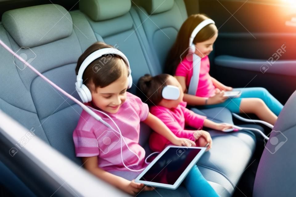 차에 앉아 헤드폰을 끼고 태블릿으로 영화를 보는 아름다운 아이들. 부모님과 함께 여행을 즐기는 어린 남매