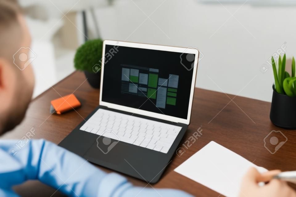 Jeune homme assis à son bureau avec son ordinateur portable et regardant les rendez-vous et les tâches de son calendrier